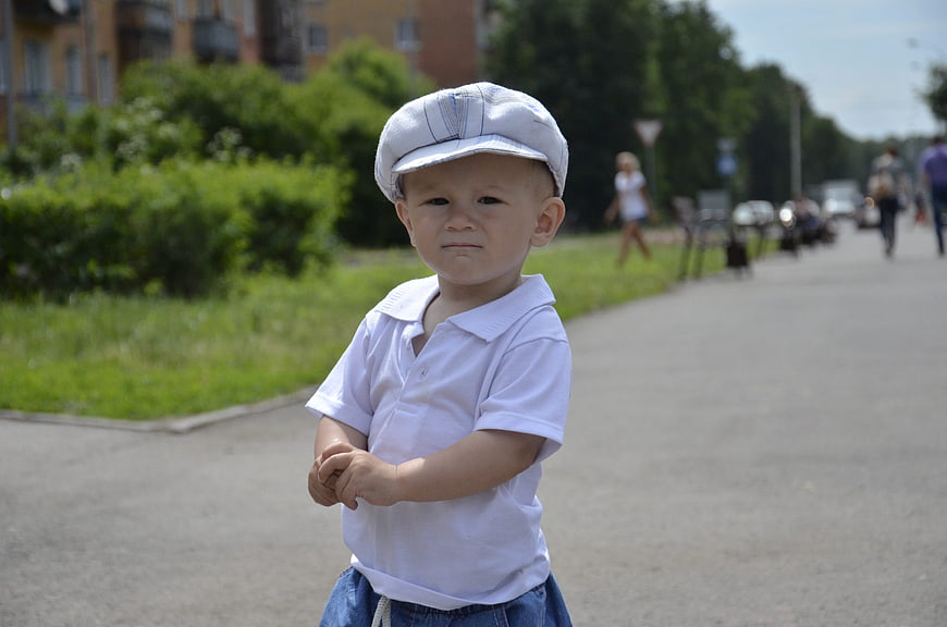 Cute toddler boy in white cap standing on sunny path