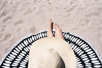 Top-down view of woman relaxing on beach towel with straw hat