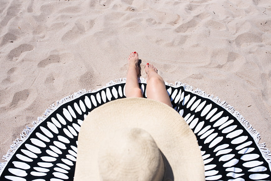Top-down view of woman relaxing on beach towel with straw hat