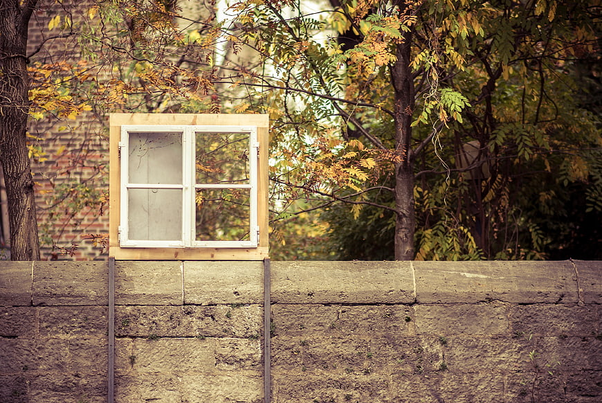 White window frame mounted on concrete wall with autumn trees