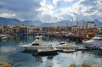 Boats docked in a scenic Mediterranean harbor with mountains