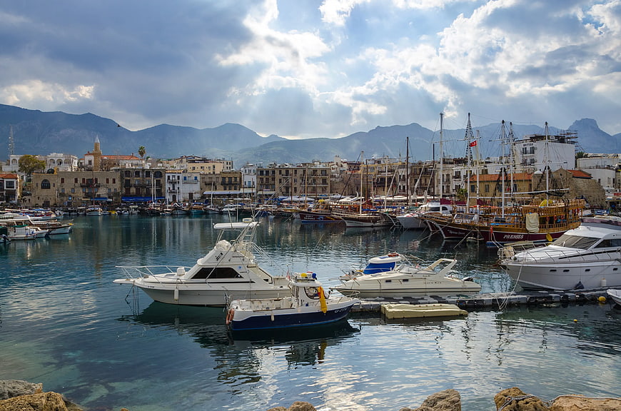 Boats docked in a scenic Mediterranean harbor with mountains