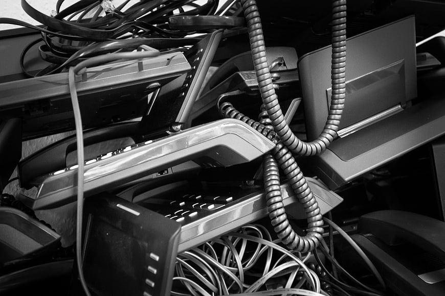 Pile of discarded old office telephones and tangled coiled cords