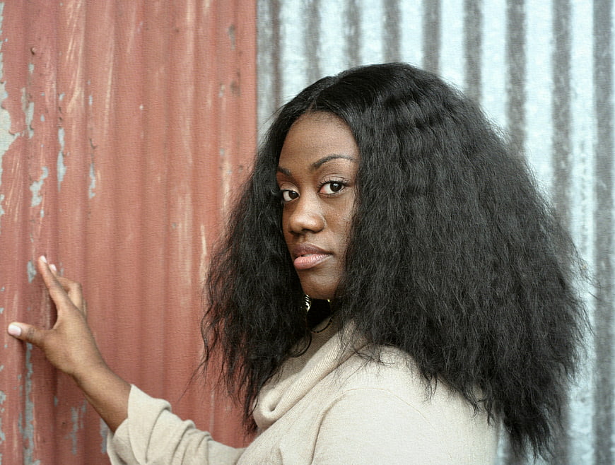 Portrait of young black woman with voluminous hair against textured wall