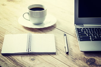 Workspace with laptop, notebook, pen, and coffee on wooden table