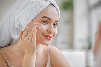 Woman applying face cream with towel on head