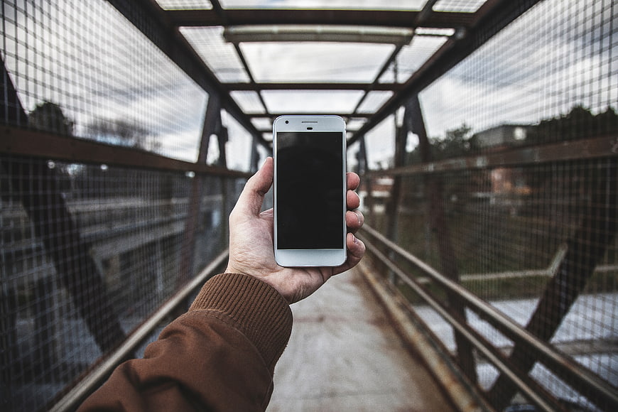 Hand holding smartphone on metal bridge