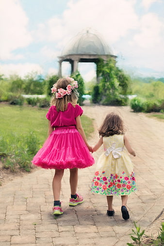 Two little girls holding hands walking away on a garden path