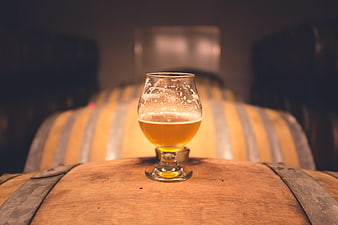 Glass of craft beer on wooden barrel in brewery