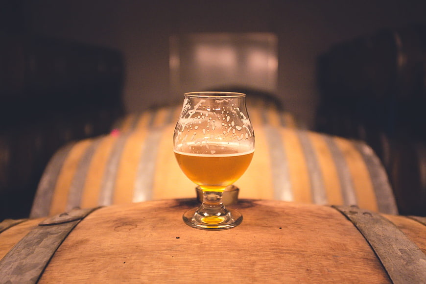 Glass of craft beer on wooden barrel in brewery