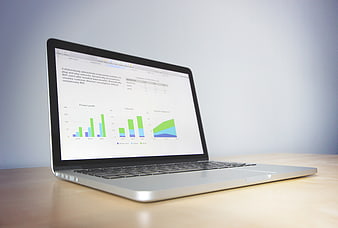Laptop displaying business charts and graphs on wooden desk