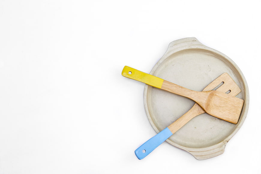 Top view of wooden spatulas in ceramic baking dish on white background