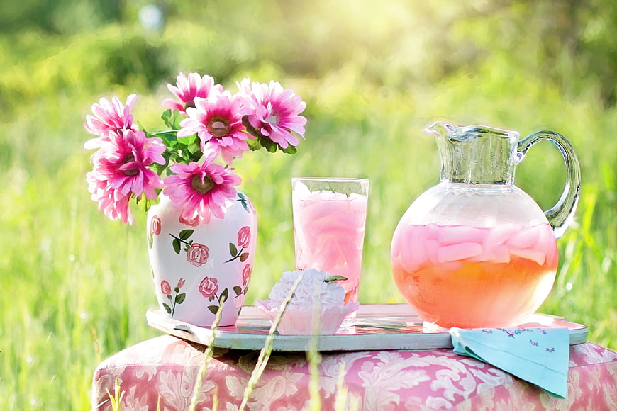 Pink lemonade pitcher and flowers on a tray in a sunny meadow