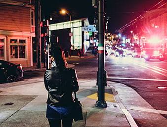Woman in leather jacket standing on city street corner at night