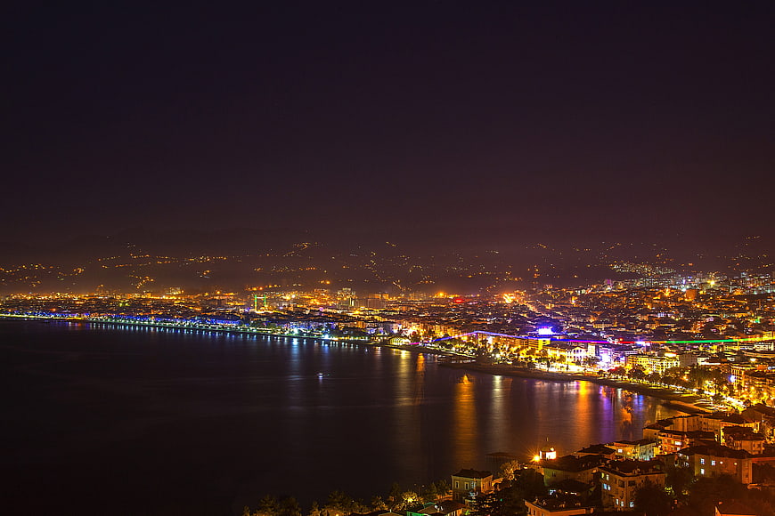 Night cityscape of coastal city with illuminated waterfront and reflections