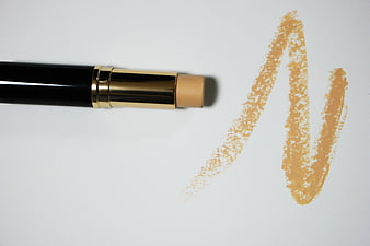 Black and gold stick foundation with beige swatch on white background