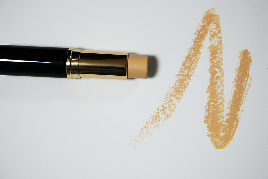 Black and gold stick foundation with beige swatch on white background