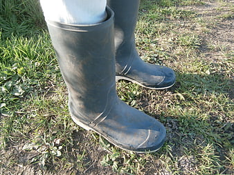 Close-up of muddy black rubber boots on grass