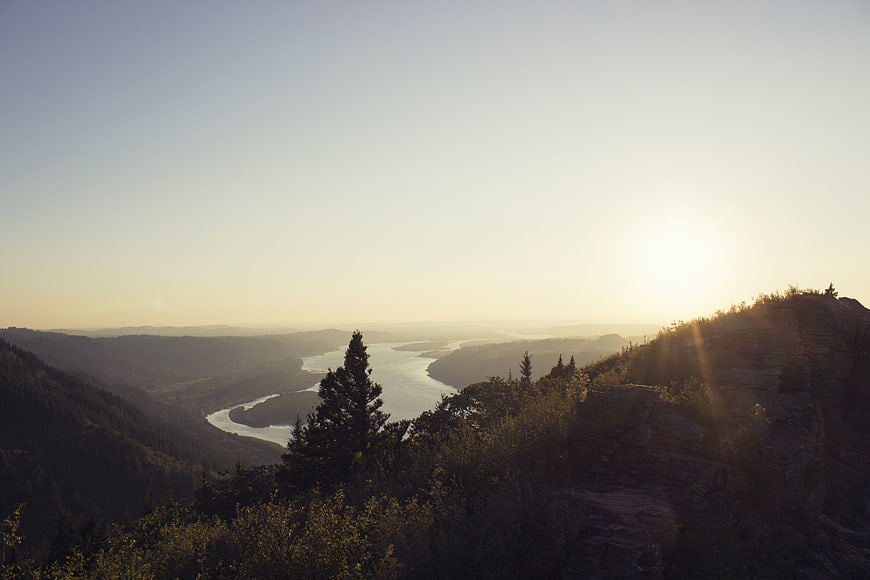 Sunset Over Winding River Valley and Forested Hills