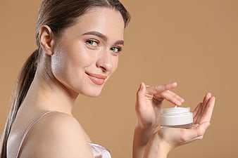 Woman with glowing skin holding cosmetic cream jar