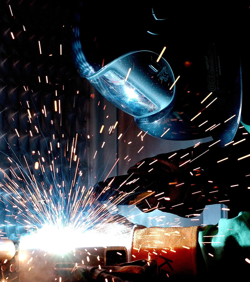 Welder in protective mask creating sparks on metal