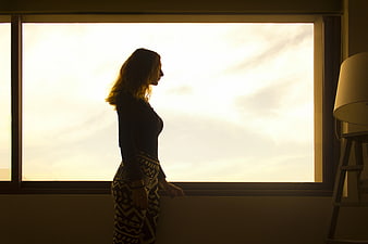 Silhouette of Woman Looking Out Window at Sunset