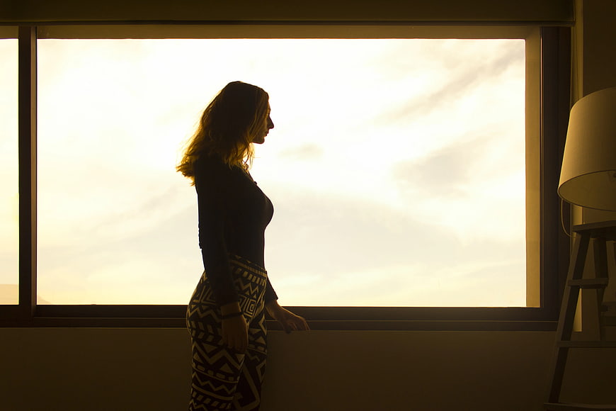 Silhouette of Woman Looking Out Window at Sunset