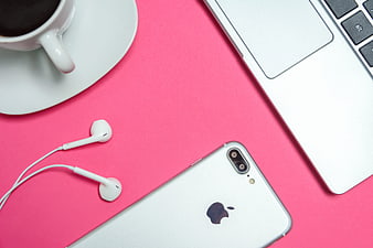 Flat lay of silver smartphone, laptop, and coffee on pink background