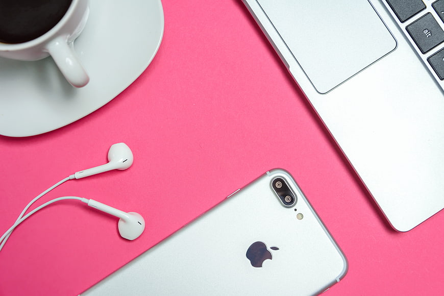 Flat lay of silver smartphone, laptop, and coffee on pink background