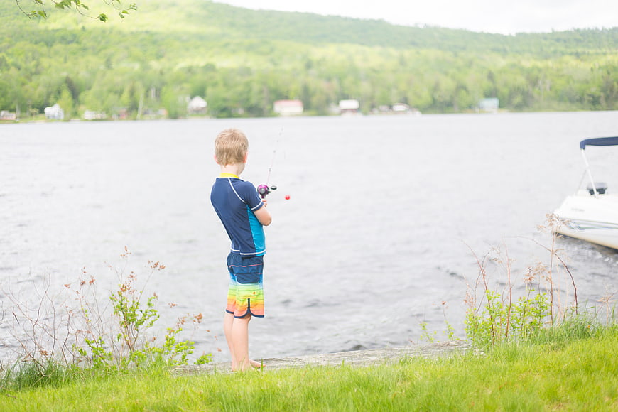 Young Boy Fishing by Lake Shore in Summer