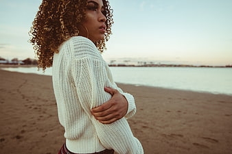 Woman with curly hair in white sweater on beach at sunset