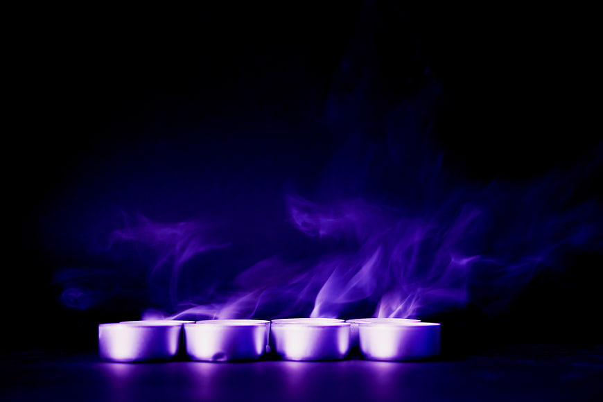 Purple tealight candles with smoke on black background