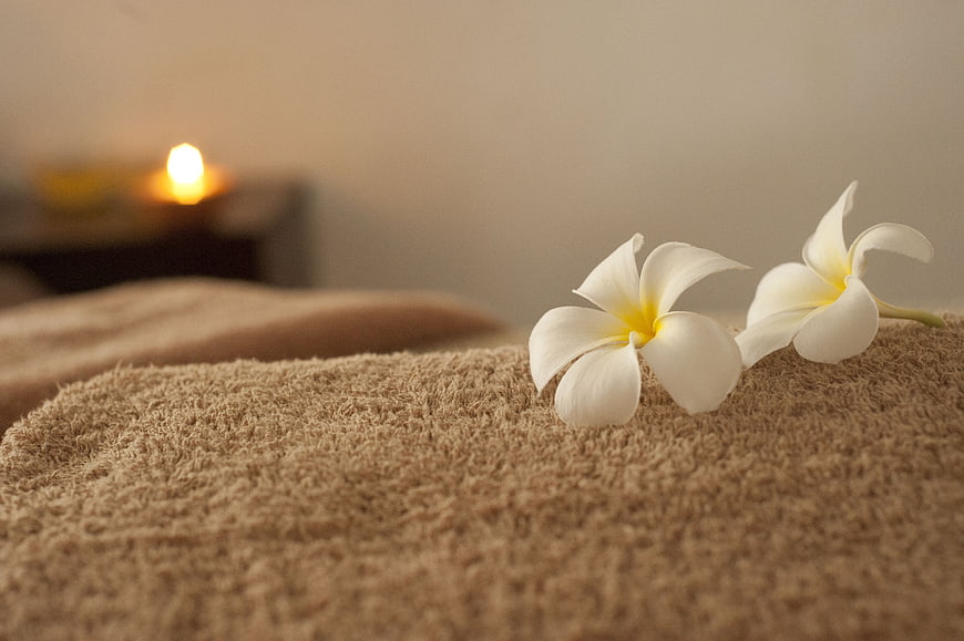 White Plumeria Flowers On Beige Spa Towel With Candlelight