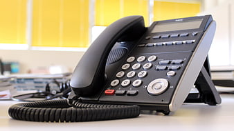 Black office telephone on desk with yellow blinds background