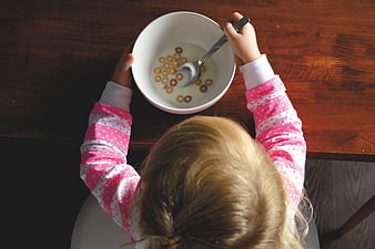 Toddler eating breakfast cereal with milk in a white bowl