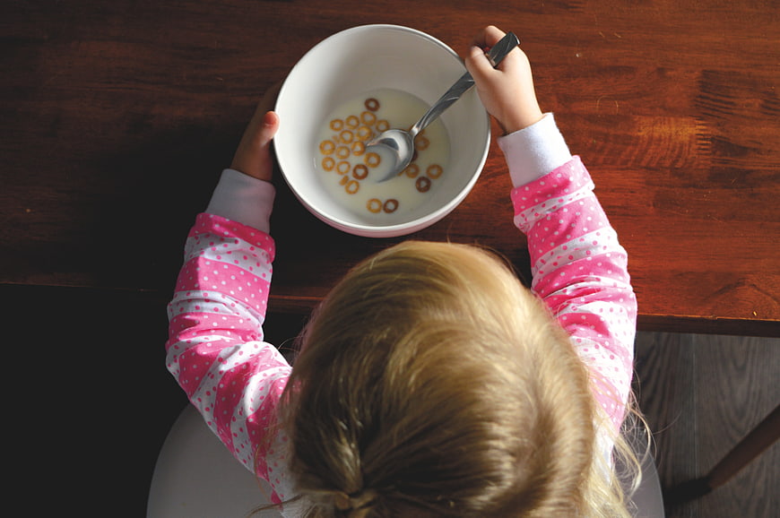 Toddler eating breakfast cereal with milk in a white bowl