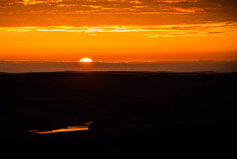 Vibrant Orange Sunrise Over Silhouetted Rolling Hills