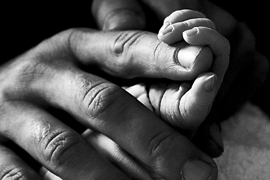 Black and white close-up of baby hand holding adult finger