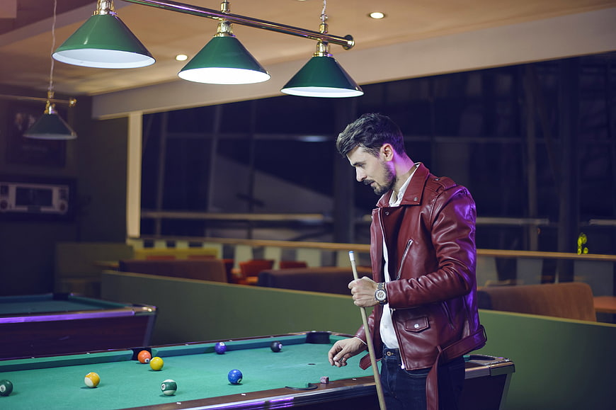 Man in red leather jacket playing pool in modern bar