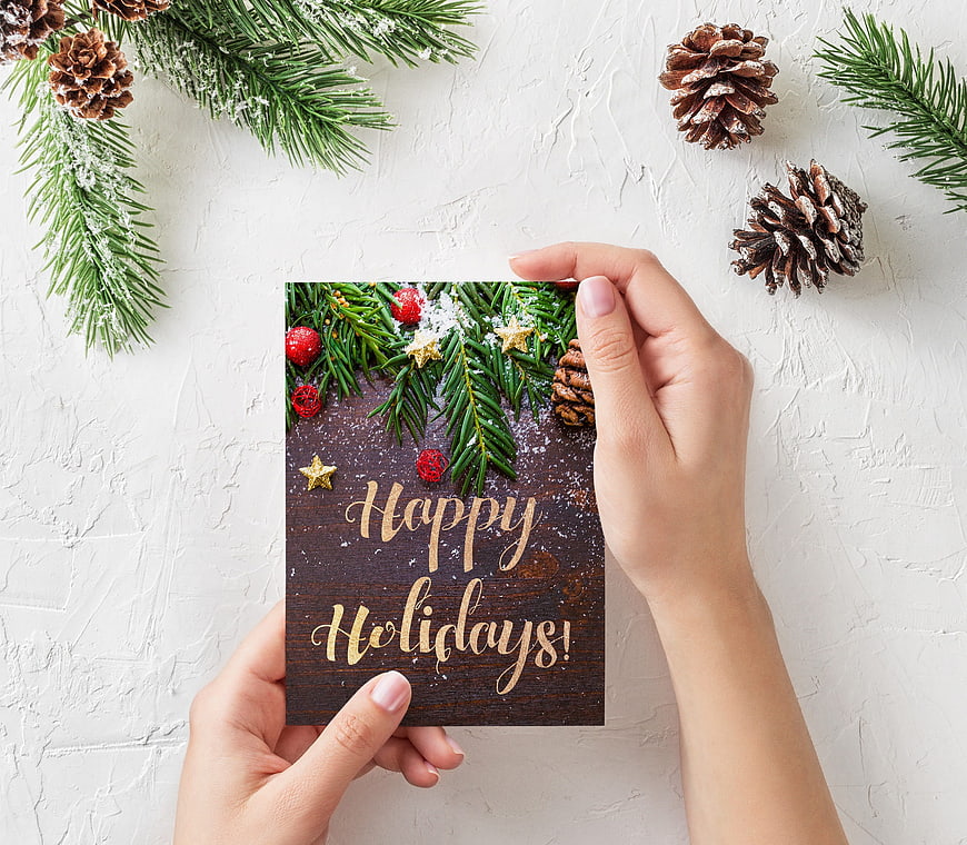 Hands holding Happy Holidays card with pine branches and cones