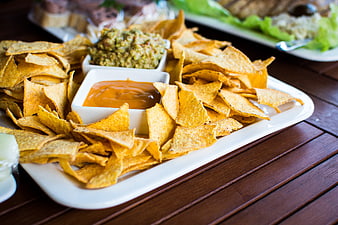 Tortilla chips with guacamole and cheese dip on wooden table