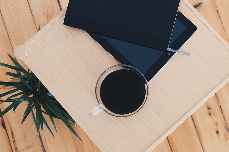 Flat lay of coffee, tablet, and notebook on wooden tray