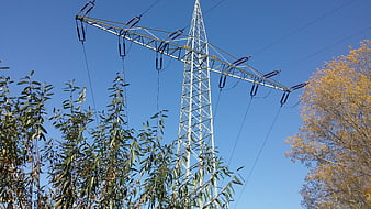 High voltage power line tower against blue sky with autumn trees