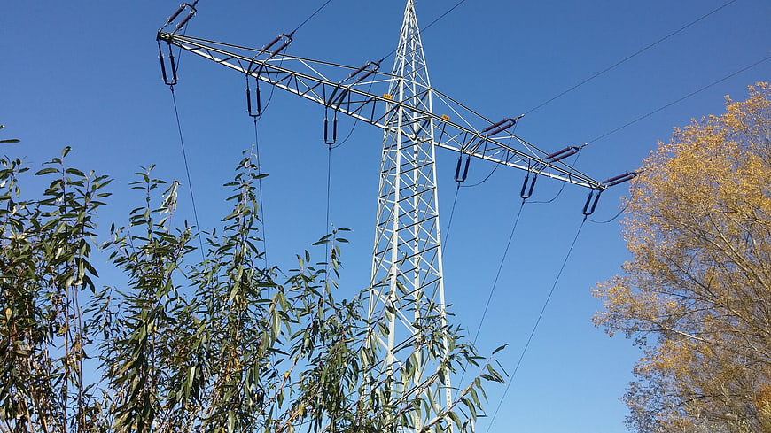 High voltage power line tower against blue sky with autumn trees