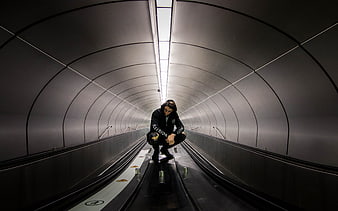 Man crouching on escalator in futuristic tunnel