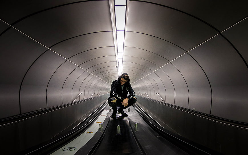 Man crouching on escalator in futuristic tunnel
