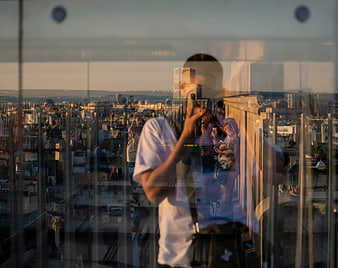 Man taking photo with reflection in glass overlooking city skyline