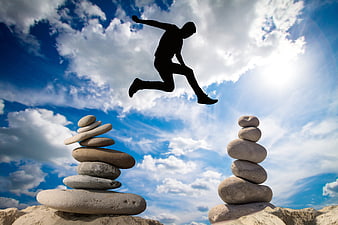 Silhouette of man jumping between stone stacks against blue sky