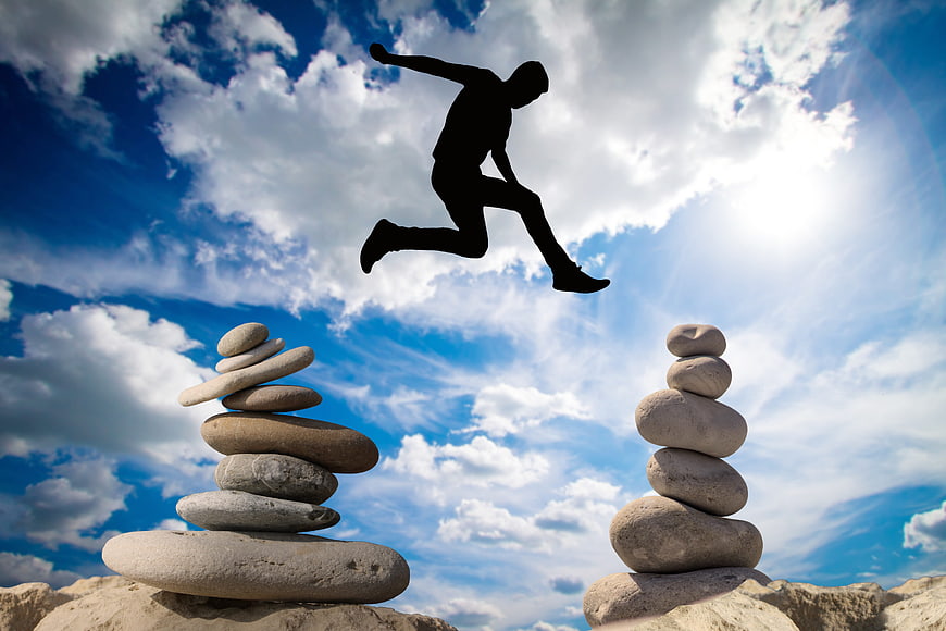 Silhouette of man jumping between stone stacks against blue sky