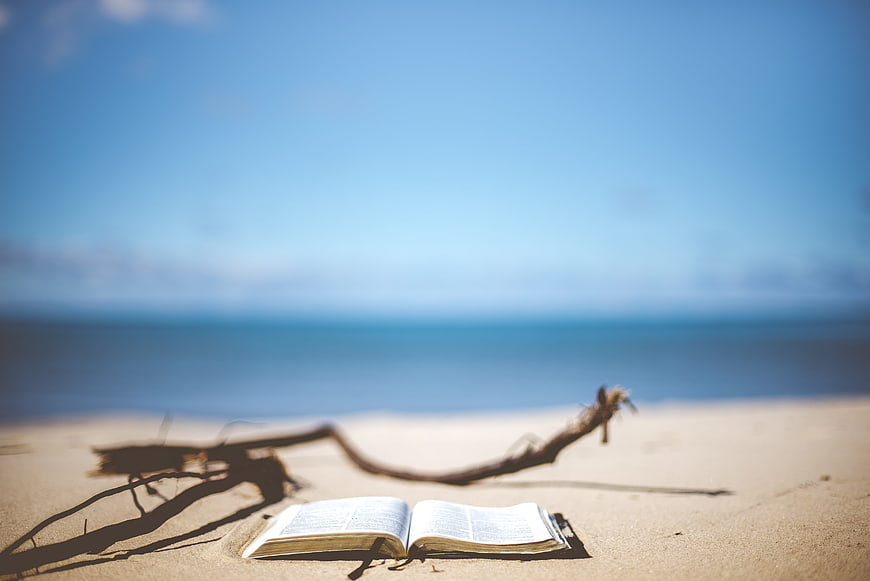 Open Bible on Sandy Beach with Ocean Background